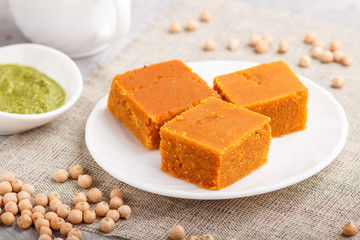 traditional indian candy burfi in white plate with mint chutney on a gray concrete background. side view.