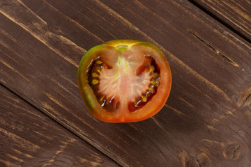 One half of fresh greenish red tomato flatlay on brown wood