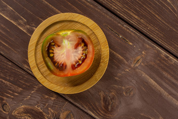 One half of fresh greenish red tomato on bamboo plate flatlay on brown wood