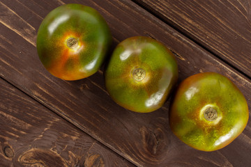 Group of three whole fresh greenish red tomato flatlay on brown wood