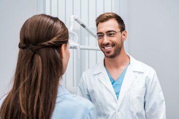 Obraz premium selective focus of cheerful dentist in glasses looking at patient in clinic