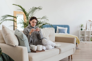 girl in a warm gray sweater knits sitting on a sofa in a cozy interior hygge