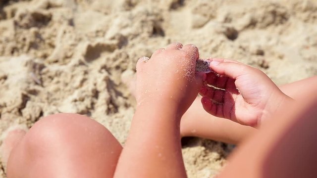 The child plays with sand on summer beach.