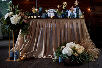 Table bride and groom at the wedding Banquet. Wedding floristry. Brown wooden screen. Tablecloth from simple tissue. Blue glass, hydrangeas , roses and cereals.