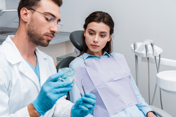 selective focus of attractive woman looking at retainer in hands of handsome dentist in glasses