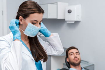 selective focus of dentist in latex gloves touching medical mask near patient