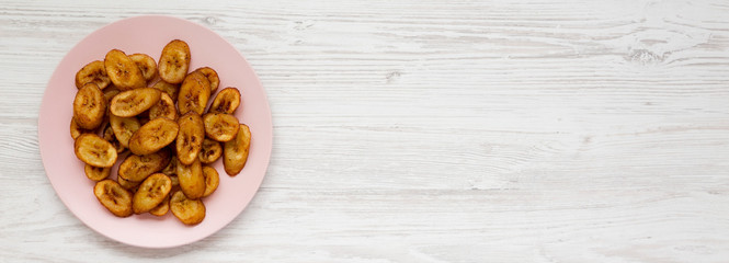 Homemade fried plantains on a pink plate over white wooden surface, top view. Flat lay, overhead, from above. Copy space.