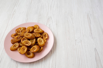 Homemade fried plantains on a pink plate on a white wooden surface, low angle view. Copy space.
