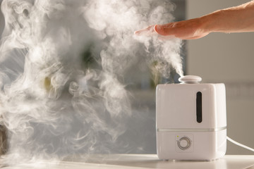 Man holds hand over steam aroma oil diffuser on the table at home, steam from the air humidifier,...