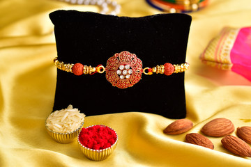 creative rakhi photoshoot on velvet cushion in golden background, raksha bandhan concept, rakhi with roli, chawal and almonds.