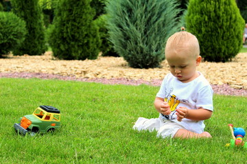 Little boy in white clothes on the green grass in the park plays with a toy on a summer day, selective focus.