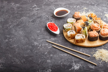 Mixed japanese maki sushi rolls set with chopsticks, ginger, soy sauce,rice on black concrete background, side view.