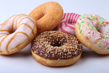 assorted delicious homemade doughnuts in the glaze, colorful sprinkles and nuts isolated on white background.