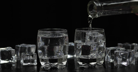 Pouring up shots of vodka from a bottle into glass. Black background