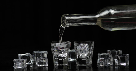Pouring up shots of vodka from a bottle into glass. Black background