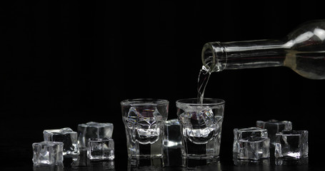 Pouring up shots of vodka from a bottle into glass. Black background