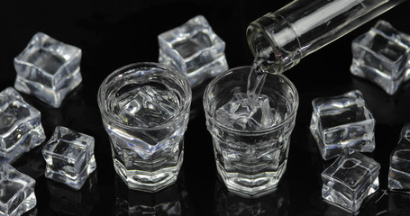 Pouring up shots of vodka from a bottle into glass. Black background