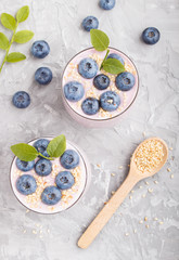 Yoghurt with blueberry and sesame in a glass and wooden spoon on gray concrete background. top view.