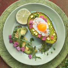 Keto diet dish: baked Avocado boat with ham cubes, quail egg and cheese served with green salad