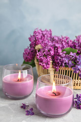 Obraz na płótnie Canvas Burning wax candles in glass holders and lilac flowers on grey table, space for text