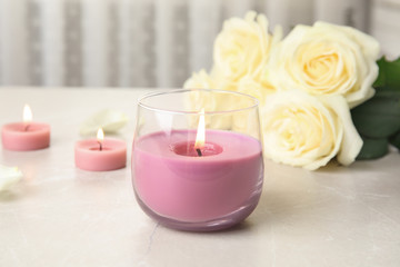 Burning candle in glass holder and roses on light table