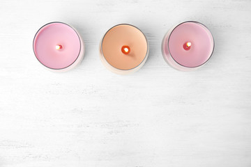 Color wax candles in glass holders on white wooden table, flat lay. Space for text