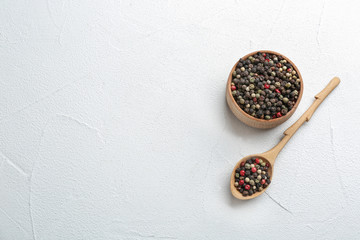 Bowl and spoon with different peppercorns on light table, top view. Space for text