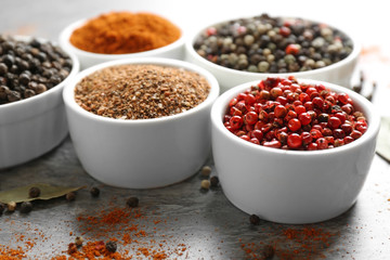 Bowls with different ground pepper and corns on grey table, closeup