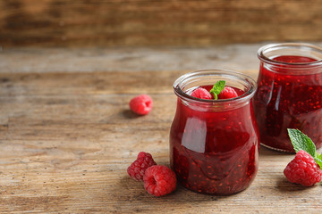 Glass jars of sweet jam with ripe raspberries and mint on wooden table. Space for text
