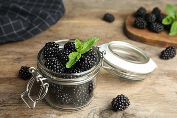 Fototapeta na wymiar Glass jar of tasty blackberries and mint on wooden table