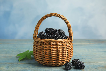 Fototapeta na wymiar Wicker basket of tasty blackberries on blue wooden table