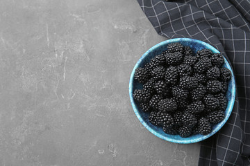 Bowl of ripe blackberries on grey table, flat lay. Space for text