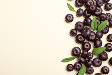 Fresh acai berries with leaves on beige background, flat lay. Space for text