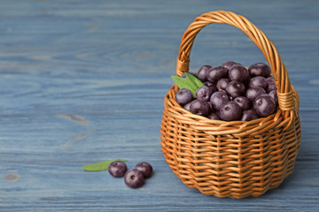 Wicker basket of fresh acai berries on blue wooden table, space for text