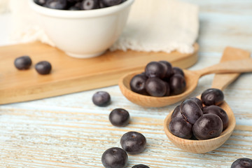 Spoons of fresh acai berries on light wooden table, closeup. Space for text