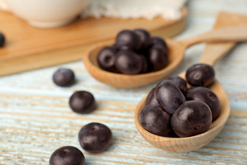 Spoons of fresh acai berries on light wooden table, closeup. Space for text
