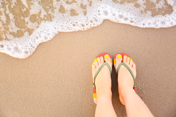 Top view of woman with stylish flip flops on sand near sea, space for text. Beach accessories
