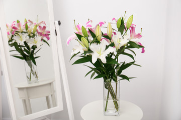 Vase with bouquet of beautiful lilies on white table near mirror