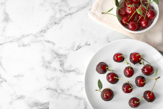Plate of chocolate dipped cherries on white marble table, flat lay. Space for text