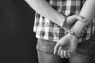 Criminal detained in handcuffs against dark background, space for text. Black and white effect