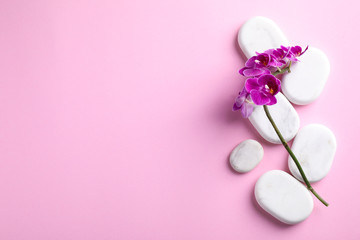 Orchid with spa stones on pink background, flat lay. Space for text