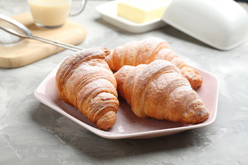 Plate of fresh croissants sprinkled with powdered sugar on grey table. French pastry