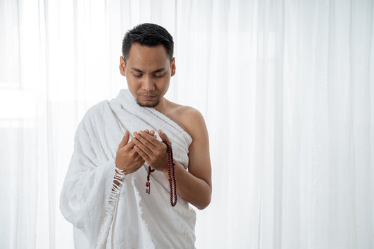 muslim young man praying using tasbih while standing in white traditional clothes