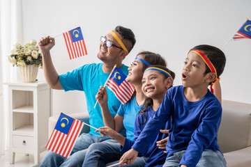 Obraz premium happy family with malaysia flag sitting on a couch watching soccer match