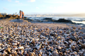 Pebbly beach in late afternoon with warm sunshine light and blurred human figures.