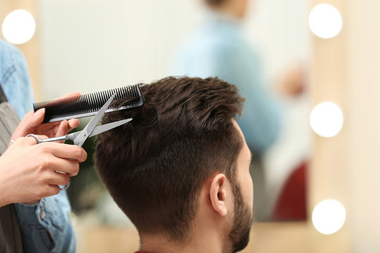 Barber making stylish haircut with professional scissors in beauty salon, closeup