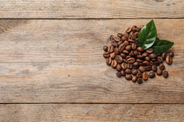 Pile of coffee beans and fresh green leaves on wooden table, top view with space for text