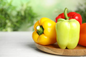 Wooden cutting board with ripe bell peppers on table against blurred background, closeup. Space for text
