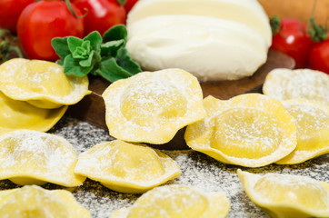 Uncooked fresh homemade ravioli stuffed next to cherry tomatoes and mozzarella