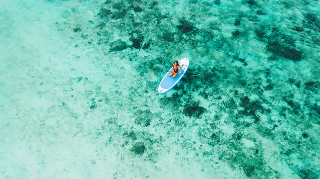 Woman sitting on sup board and enjoying turquoise transparent water and coral reef. Tropical travel, wanderlust and water activity concept.